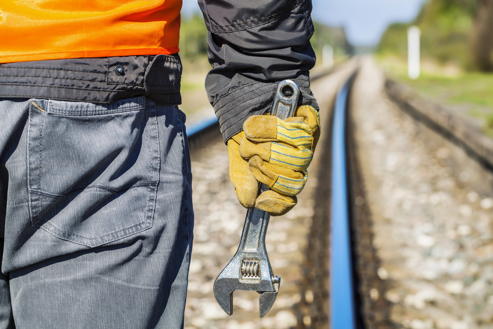 railroad worker with adjustable wrench on railway in spring