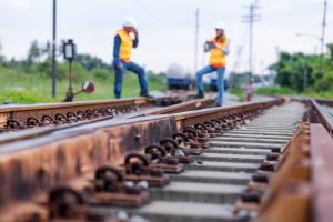 Two engineers wearing safety gear and clothing inspect the tracks of a natural gas transport train